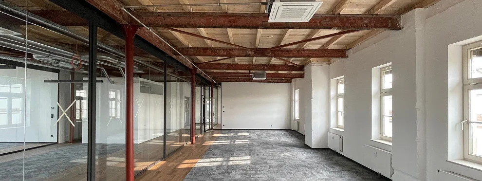 Offene Bürofläche im Alten Lager mit sichtbarem Holzdachstuhl, roten Stahlstützen und Glastrennwänden