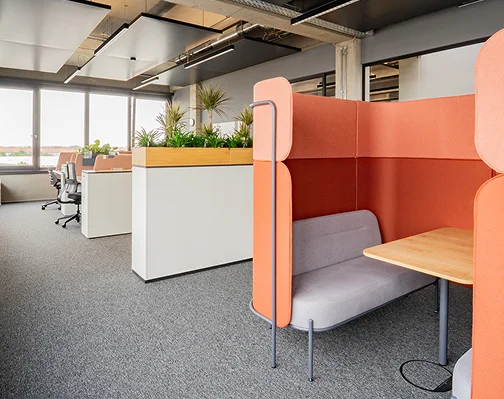 Meetingbereich im Neubau mit orangefarbener Akustik-Sitznische, Pflanzeninsel und offenen Arbeitsplätzen