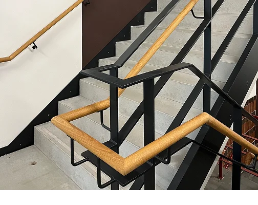 Treppenhaus im Neubau mit schwarzem Stahlgeländer und hellem Holzhandlauf