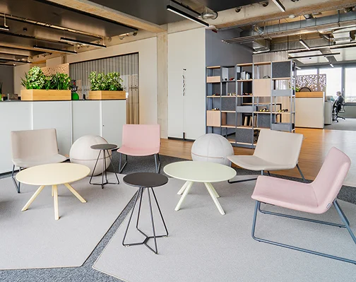 Lounge im Neubau mit gepolsterten Sesseln in Pastelltönen, runden Beistelltischen und Bücherregal