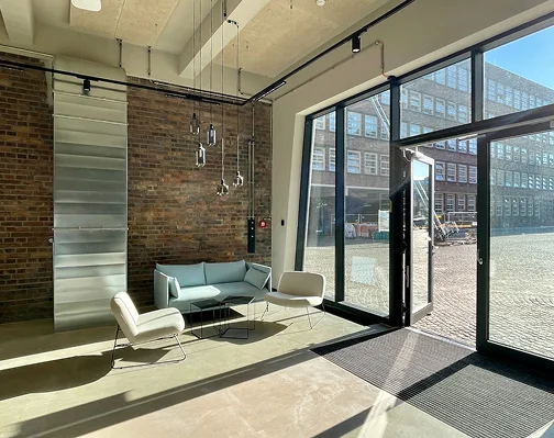 Foyer der Werkstatt mit Ziegelwand, raumhoher Glasfront und Sitzgruppe